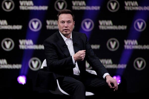 Elon Musk, the owner of Twitter and SpaceX and chief executive of Tesla, wearing a white-button down shirt and black suit. He has a mic pinned to his shirt.